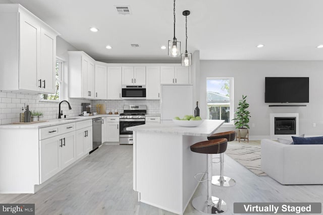 kitchen with white cabinets, light hardwood / wood-style flooring, a kitchen island, and appliances with stainless steel finishes