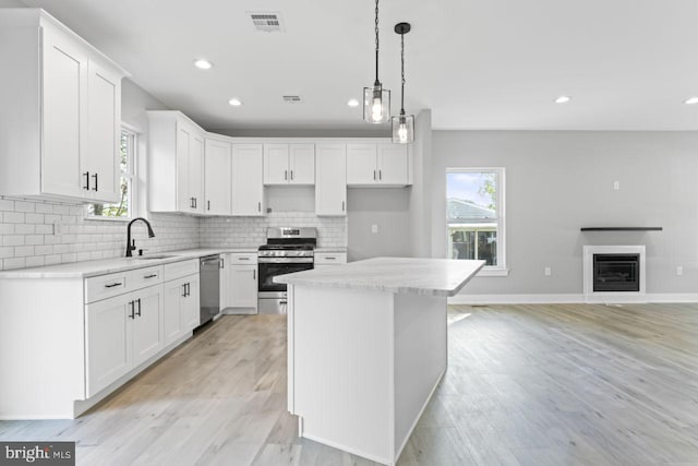 kitchen featuring white cabinets, appliances with stainless steel finishes, a center island, and light hardwood / wood-style flooring