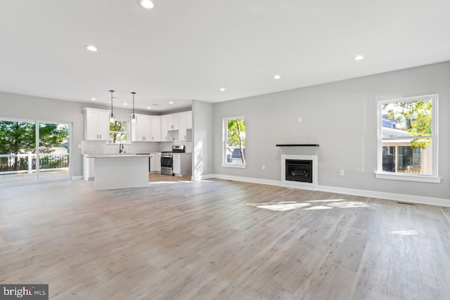 unfurnished living room with a healthy amount of sunlight, light hardwood / wood-style floors, and sink