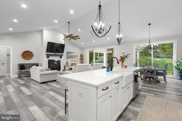 kitchen featuring dishwasher, an island with sink, a large fireplace, hanging light fixtures, and white cabinetry