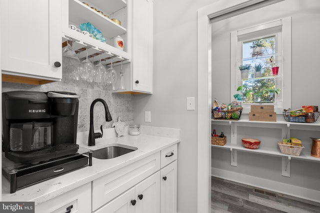 kitchen featuring hardwood / wood-style floors, sink, light stone countertops, white cabinets, and tasteful backsplash