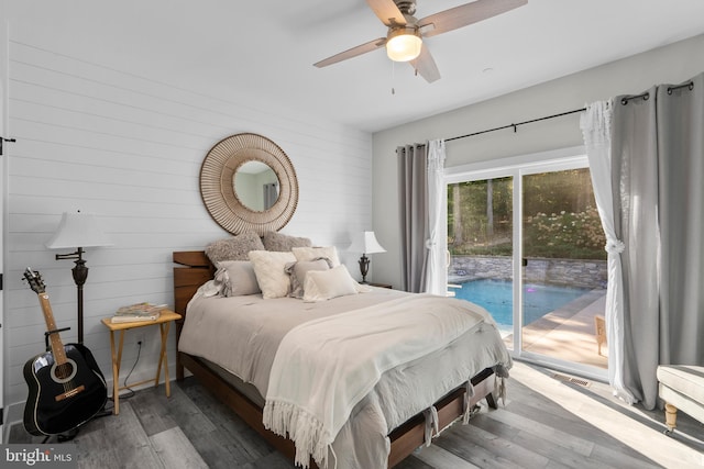 bedroom featuring wood walls, access to exterior, wood-type flooring, and ceiling fan