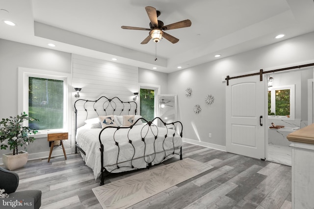 bedroom featuring ceiling fan, hardwood / wood-style flooring, multiple windows, and a barn door