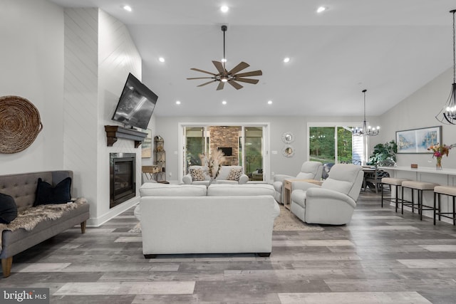 living room with light hardwood / wood-style floors, high vaulted ceiling, ceiling fan with notable chandelier, and a fireplace