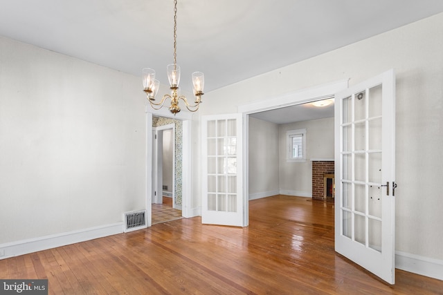 unfurnished dining area with a fireplace, wood-type flooring, french doors, and a notable chandelier