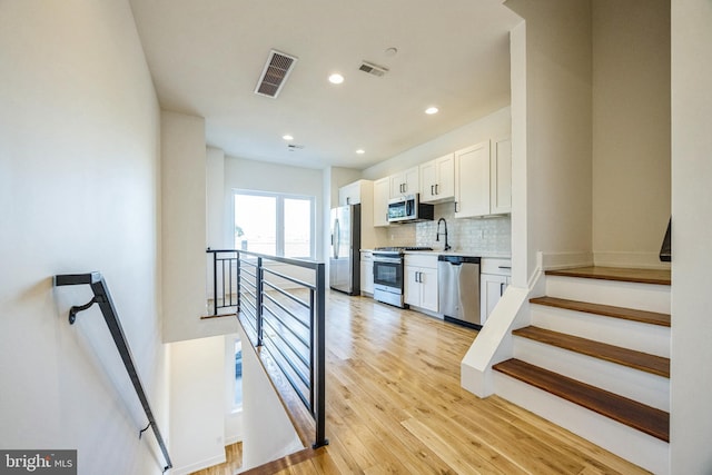 kitchen featuring sink, light hardwood / wood-style flooring, decorative backsplash, appliances with stainless steel finishes, and white cabinetry