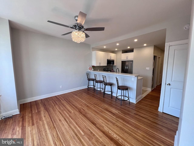 kitchen featuring hardwood / wood-style floors, a breakfast bar, kitchen peninsula, appliances with stainless steel finishes, and white cabinetry