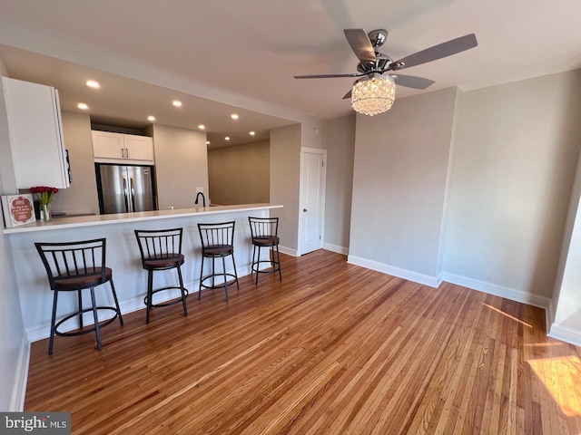 kitchen featuring stainless steel refrigerator, kitchen peninsula, a kitchen bar, white cabinets, and light wood-type flooring