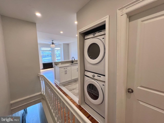 laundry area with sink, ceiling fan, stacked washing maching and dryer, light hardwood / wood-style floors, and radiator heating unit