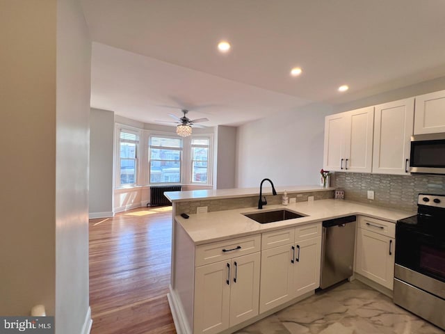 kitchen with kitchen peninsula, sink, light wood-type flooring, appliances with stainless steel finishes, and white cabinetry