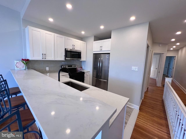 kitchen featuring a breakfast bar, white cabinets, hardwood / wood-style flooring, kitchen peninsula, and stainless steel appliances