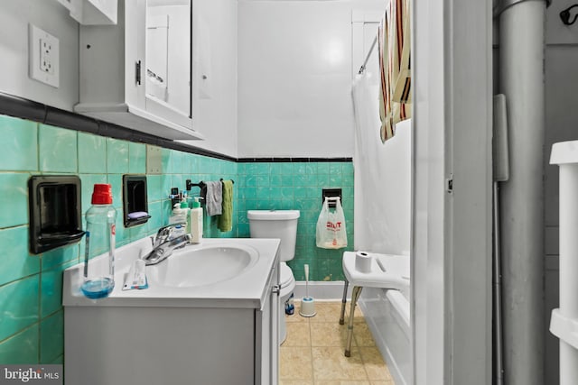 bathroom with a shower with shower curtain, toilet, tile patterned floors, tile walls, and vanity