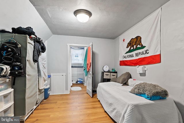 bedroom with hardwood / wood-style flooring, a textured ceiling, and vaulted ceiling