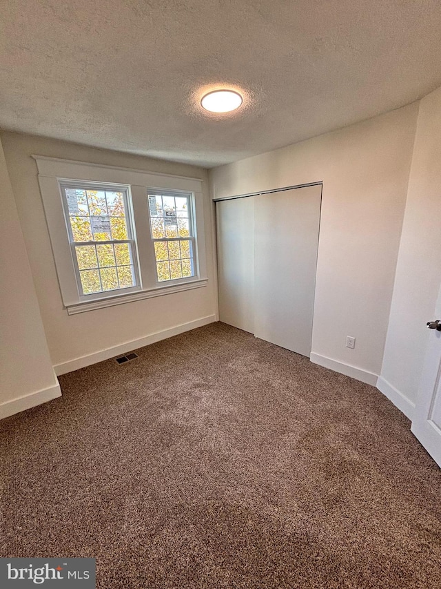 unfurnished bedroom with a closet, a textured ceiling, and dark carpet