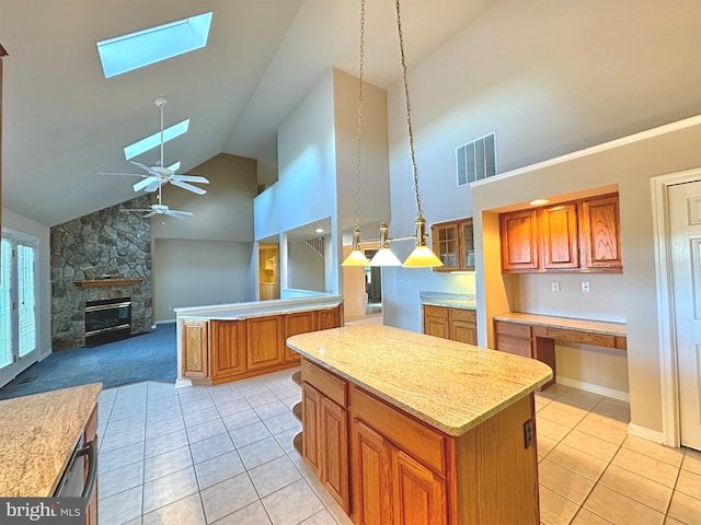 kitchen featuring a kitchen island, a stone fireplace, pendant lighting, high vaulted ceiling, and a skylight