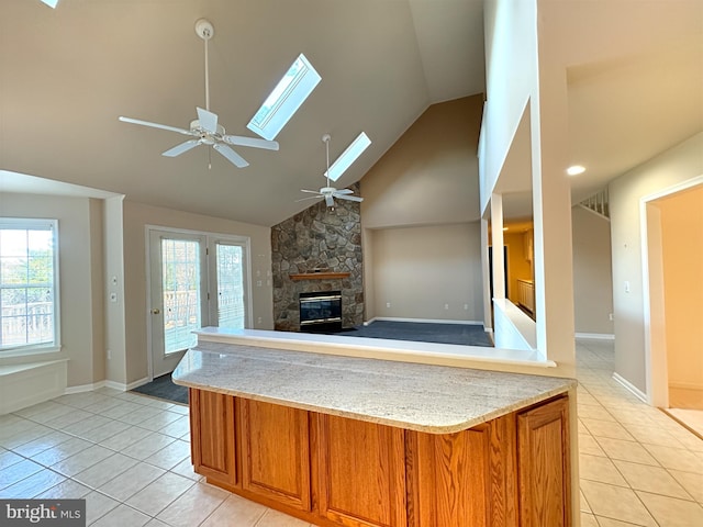 kitchen with light tile patterned floors, a skylight, a fireplace, high vaulted ceiling, and ceiling fan