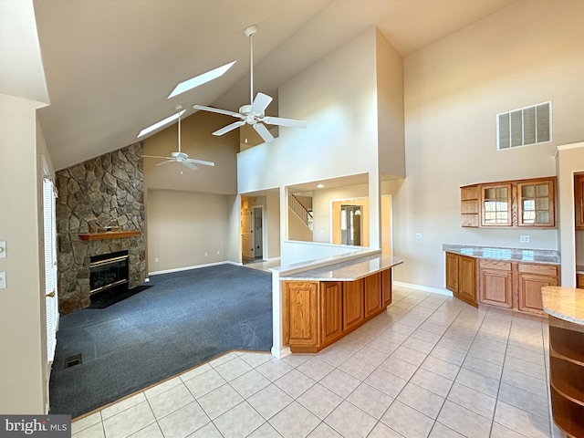 kitchen featuring a skylight, a fireplace, light carpet, ceiling fan, and high vaulted ceiling