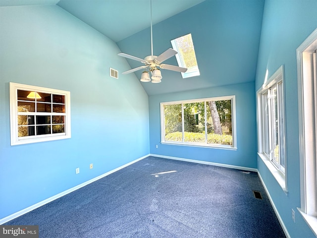 empty room with dark carpet, high vaulted ceiling, a skylight, and ceiling fan