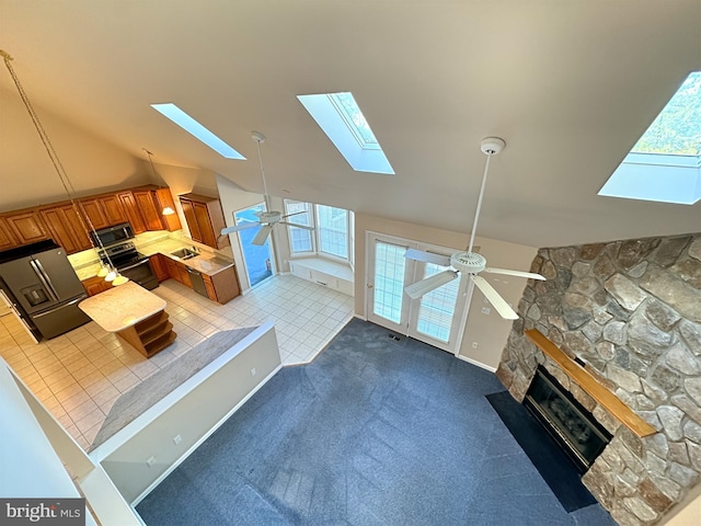 living room with a skylight, a stone fireplace, ceiling fan, tile patterned floors, and high vaulted ceiling