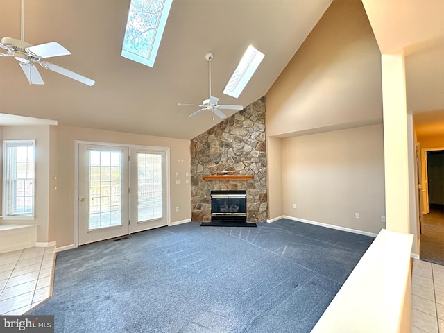 carpeted living room with ceiling fan, high vaulted ceiling, a skylight, and a stone fireplace