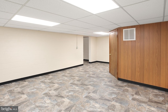 basement featuring a paneled ceiling and wood walls