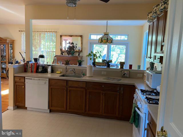 kitchen with decorative light fixtures, kitchen peninsula, sink, and white appliances