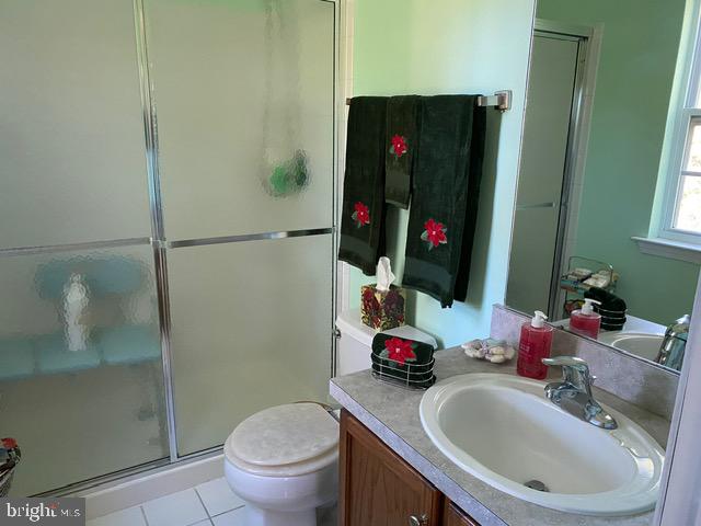 bathroom with a shower with door, tile patterned floors, vanity, and toilet