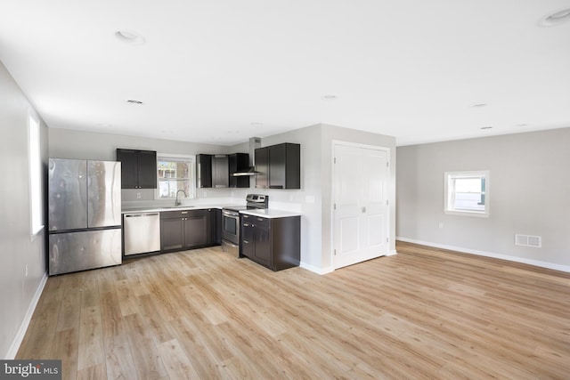 kitchen featuring light hardwood / wood-style floors, stainless steel appliances, wall chimney range hood, and a wealth of natural light