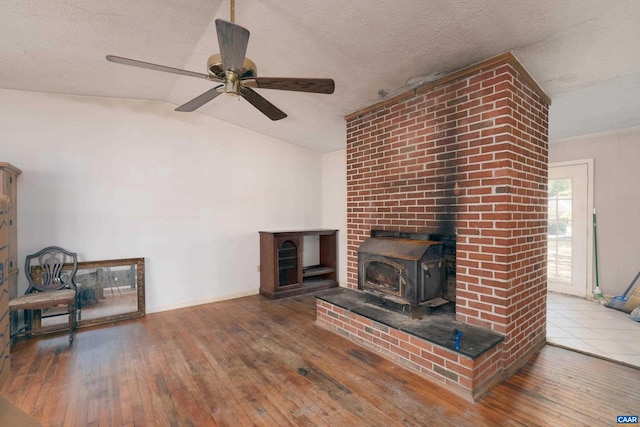 living room featuring ceiling fan, a wood stove, wood-type flooring, a textured ceiling, and vaulted ceiling