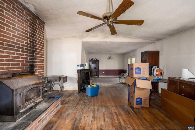 interior space featuring ceiling fan, dark hardwood / wood-style flooring, vaulted ceiling, a wood stove, and a textured ceiling