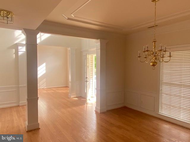 spare room featuring crown molding, a notable chandelier, hardwood / wood-style floors, and ornate columns