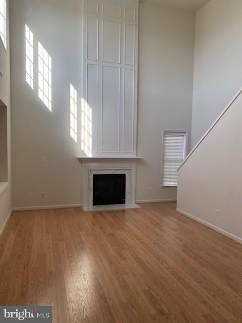 unfurnished living room featuring hardwood / wood-style flooring, a large fireplace, and a high ceiling