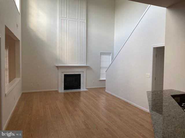 unfurnished living room with a towering ceiling, a fireplace, and light hardwood / wood-style flooring