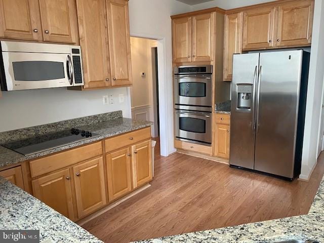 kitchen with stainless steel appliances, light stone counters, and light hardwood / wood-style floors