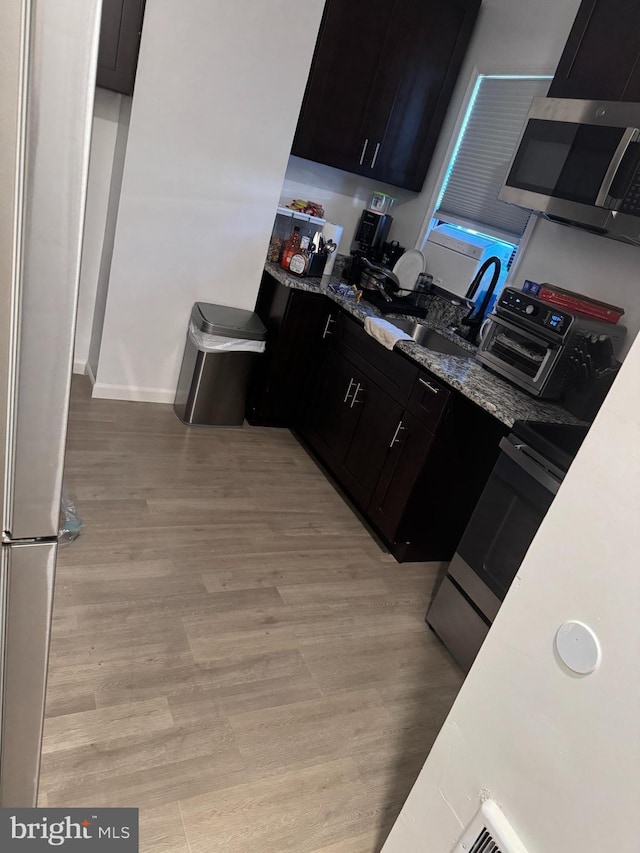 kitchen featuring sink, light wood-type flooring, stone countertops, and appliances with stainless steel finishes