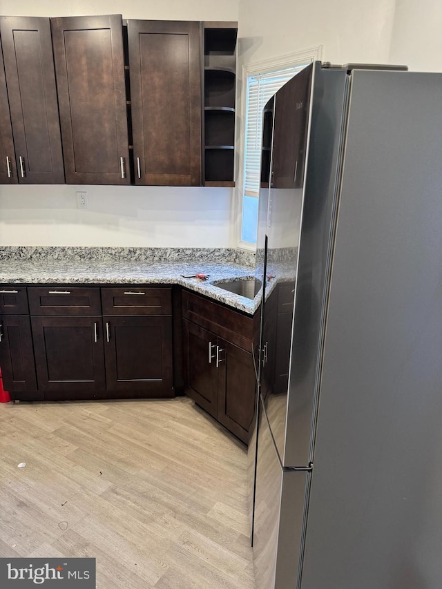 kitchen with sink, light wood-type flooring, light stone countertops, dark brown cabinetry, and stainless steel refrigerator