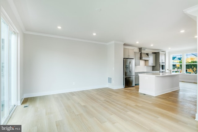 kitchen featuring a center island with sink, stainless steel appliances, custom range hood, and light hardwood / wood-style flooring