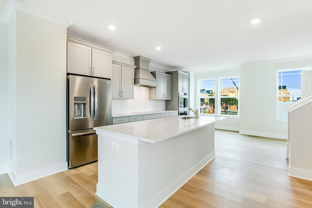 kitchen with gray cabinetry, light hardwood / wood-style flooring, a center island with sink, appliances with stainless steel finishes, and premium range hood