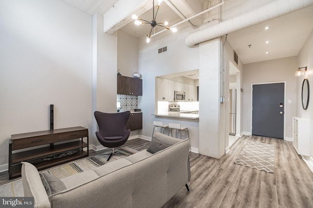 living room featuring beamed ceiling, light wood-type flooring, a towering ceiling, and a chandelier