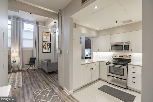 kitchen featuring white cabinets, backsplash, appliances with stainless steel finishes, and light wood-type flooring