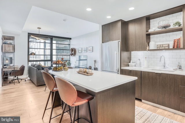 kitchen with stainless steel refrigerator, decorative backsplash, sink, light hardwood / wood-style floors, and a breakfast bar