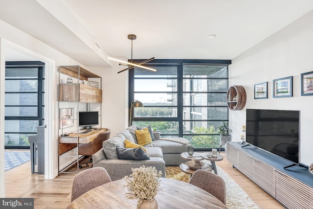 living room featuring light wood-type flooring, a wall of windows, and a notable chandelier