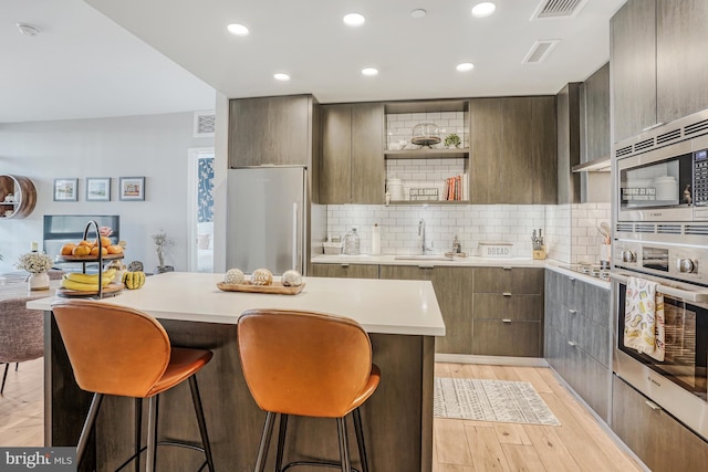 kitchen with light wood-type flooring, appliances with stainless steel finishes, backsplash, sink, and a breakfast bar area