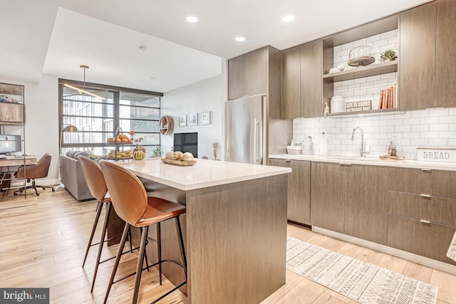 kitchen with sink, a kitchen island, stainless steel refrigerator, a breakfast bar, and light hardwood / wood-style flooring