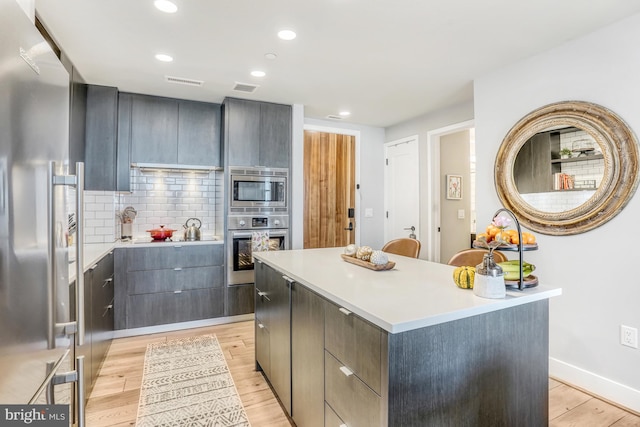 kitchen featuring appliances with stainless steel finishes, tasteful backsplash, a kitchen island, and light hardwood / wood-style flooring