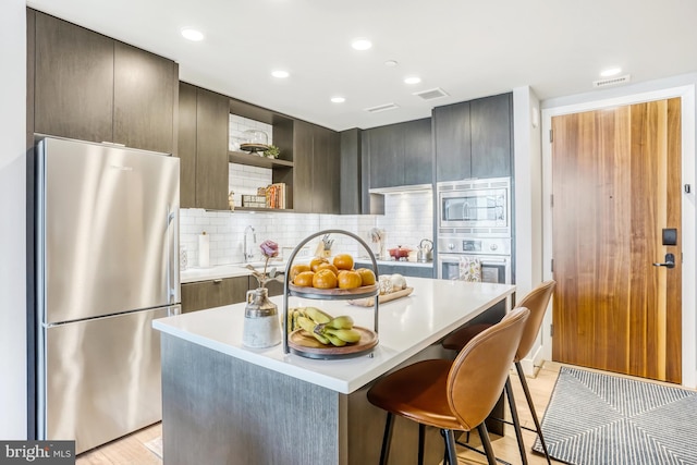 kitchen with appliances with stainless steel finishes, a kitchen bar, backsplash, light hardwood / wood-style flooring, and a kitchen island