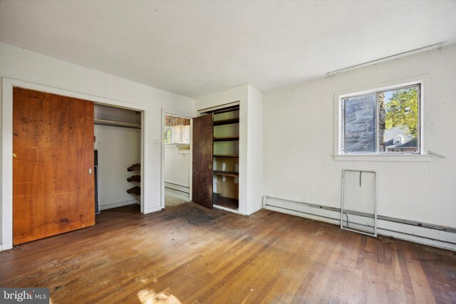 unfurnished bedroom featuring a closet, hardwood / wood-style floors, and a baseboard heating unit