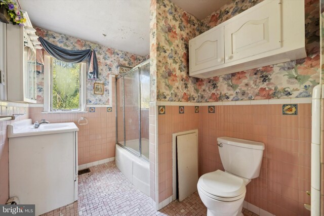 full bathroom featuring toilet, tile patterned flooring, vanity, tile walls, and shower / bath combination with glass door