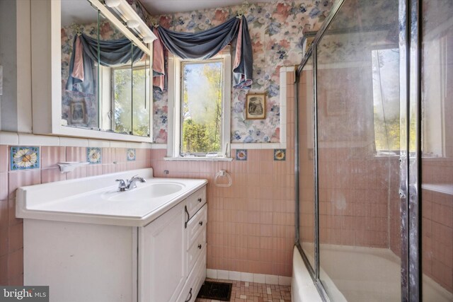 bathroom featuring tile walls, vanity, and shower / bath combination with glass door