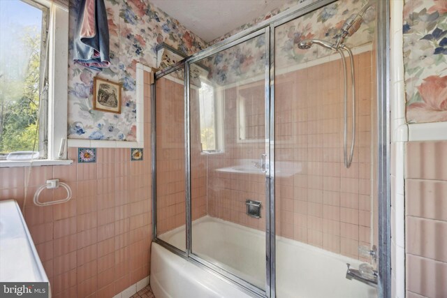 bathroom featuring tile walls and bath / shower combo with glass door